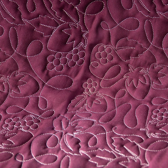 Close-up of a purple fabric with machine embroidery berries and floral design