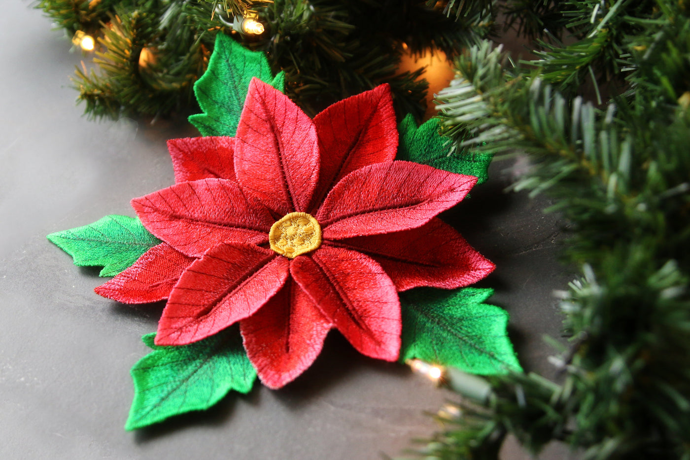 Machine embroidered Red poinsettia freestanding flower with green leaves near a Christmas tree