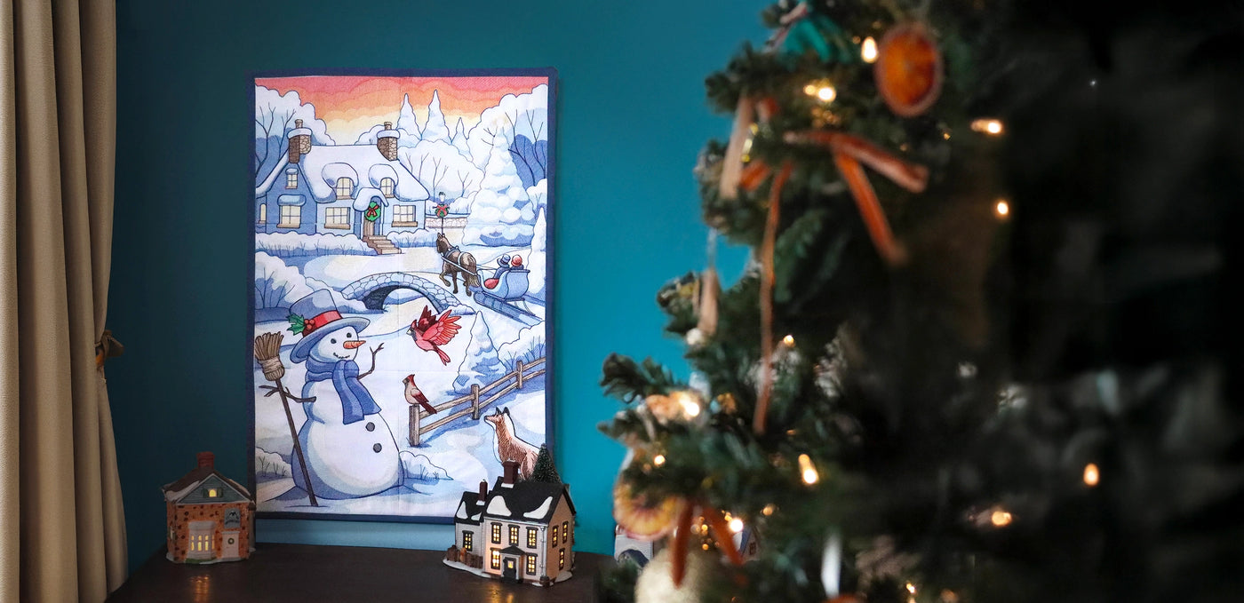 Decorative machine embroidered Christmas scene featuring a snowy village, snowman, and horse drawn sleigh.