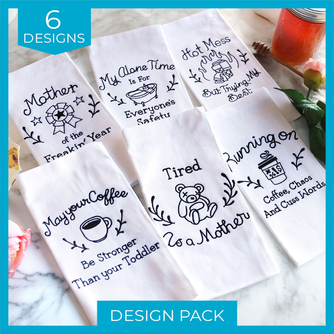 Six white cloths, each embroidered with a different humorous mom saying in colorful thread, are laid out side by side.