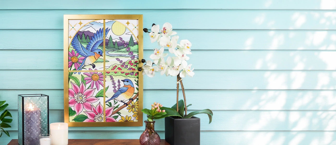 Decorative wall art with machine embroidery birds and flowers on a wooden surface against a light blue wall.