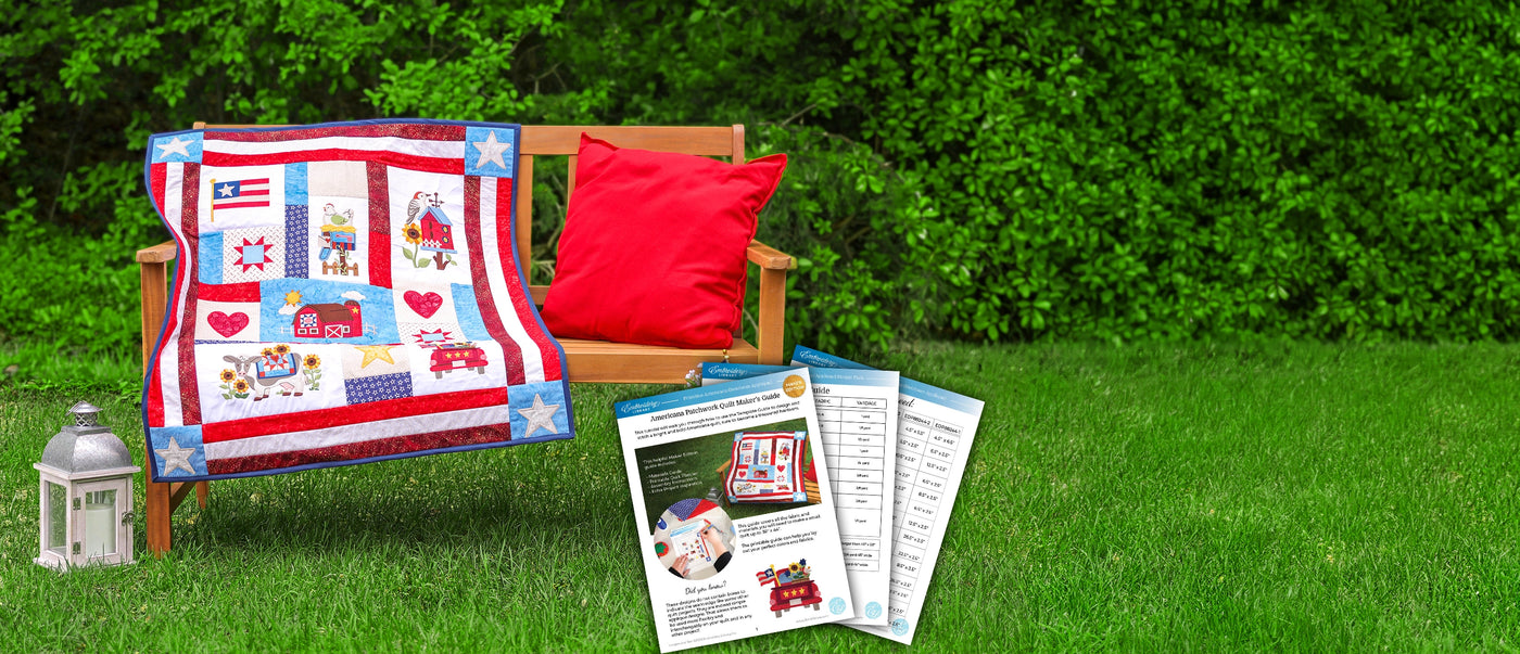 Quilt with machine embroidered patriotic designs on a bench outdoors, with brochures and a lantern nearby.