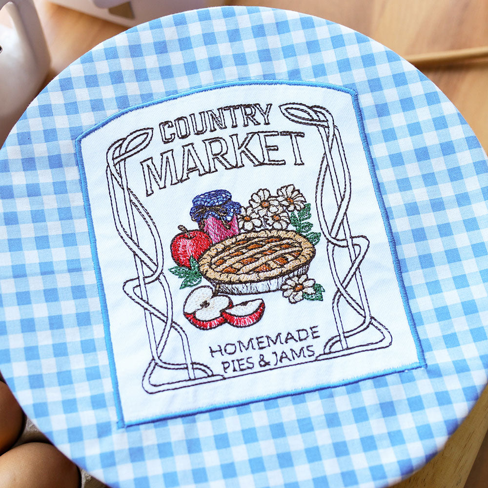 Embroidery design showing a circular motif with an apple pie, assorted fruits, and flowers; digitally downloadable design.