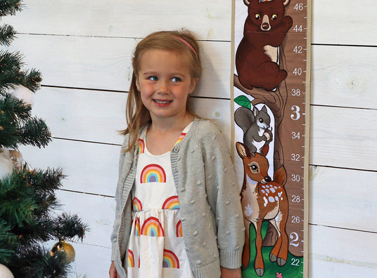 Child standing next to a machine embroidered growth chart with animals on a wooden background