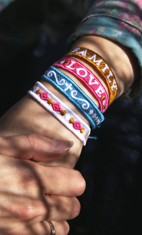 Close-up of a wrist wearing colorful machine embroidered bracelets with text on a dark background