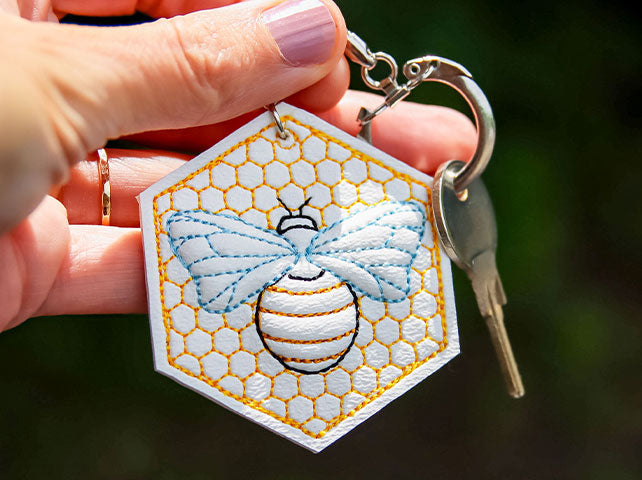 hand holding completed embroidered puff underlay keychain, featuring Buzzing Bee design