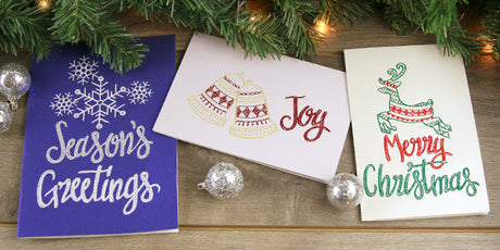 Machine embroidered cardstock greeting cards - one on blue cardstock with snowflakes and phrase Season Greetings - one on white cardstock with bells and phrase Joy - one on white cardstock with reindeer with phrase Merry Christmas