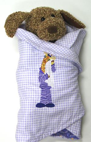 Plush dog wrapped in Embroidered Baby Swaddler, featuring Giraffe in Pajamas design
