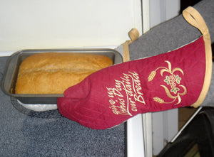 a pair of hands putting baked bread on the counter, wearing the finished Embroidered Oven Mitts