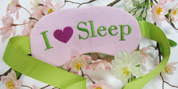 Completed Sleep Mask project with 'I (Heart) Sleep' design, flowers in the background