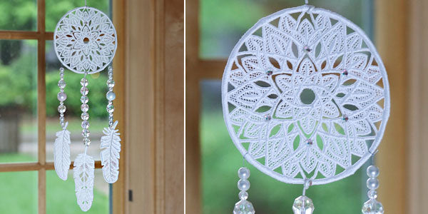 Completed lace dream catcher with three feather pendants hanging in a window