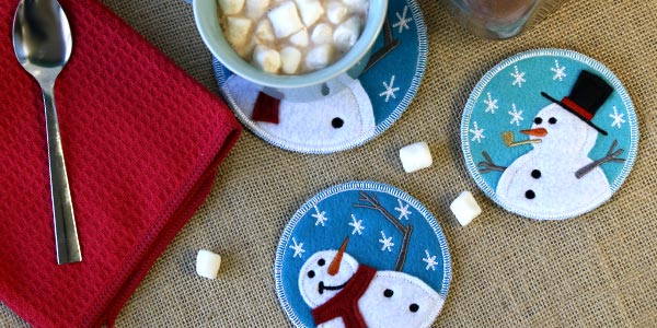Completed snowman applique coasters with a mug of hot chocolate