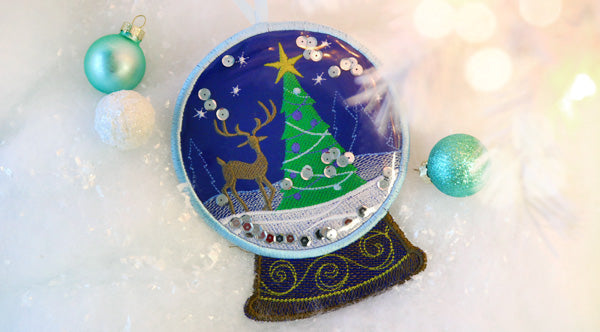 Completed Reindeer Snowglobe  Ornament project surrounded by snow and bulb ornaments