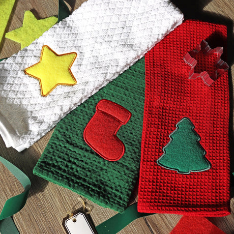 Machine embroidered Christmas star, stocking, and tree applique designs on tea towels.