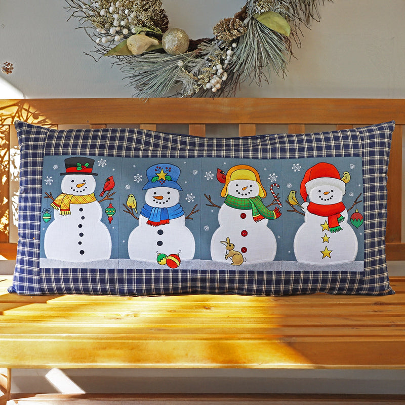 Decorative machine embroidered pillow featuring applique winter snowman design on a wooden bench