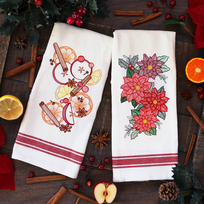 Two embroidered towels with designs of fall spices and Christmas poinsettias on a wooden surface with festive elements.