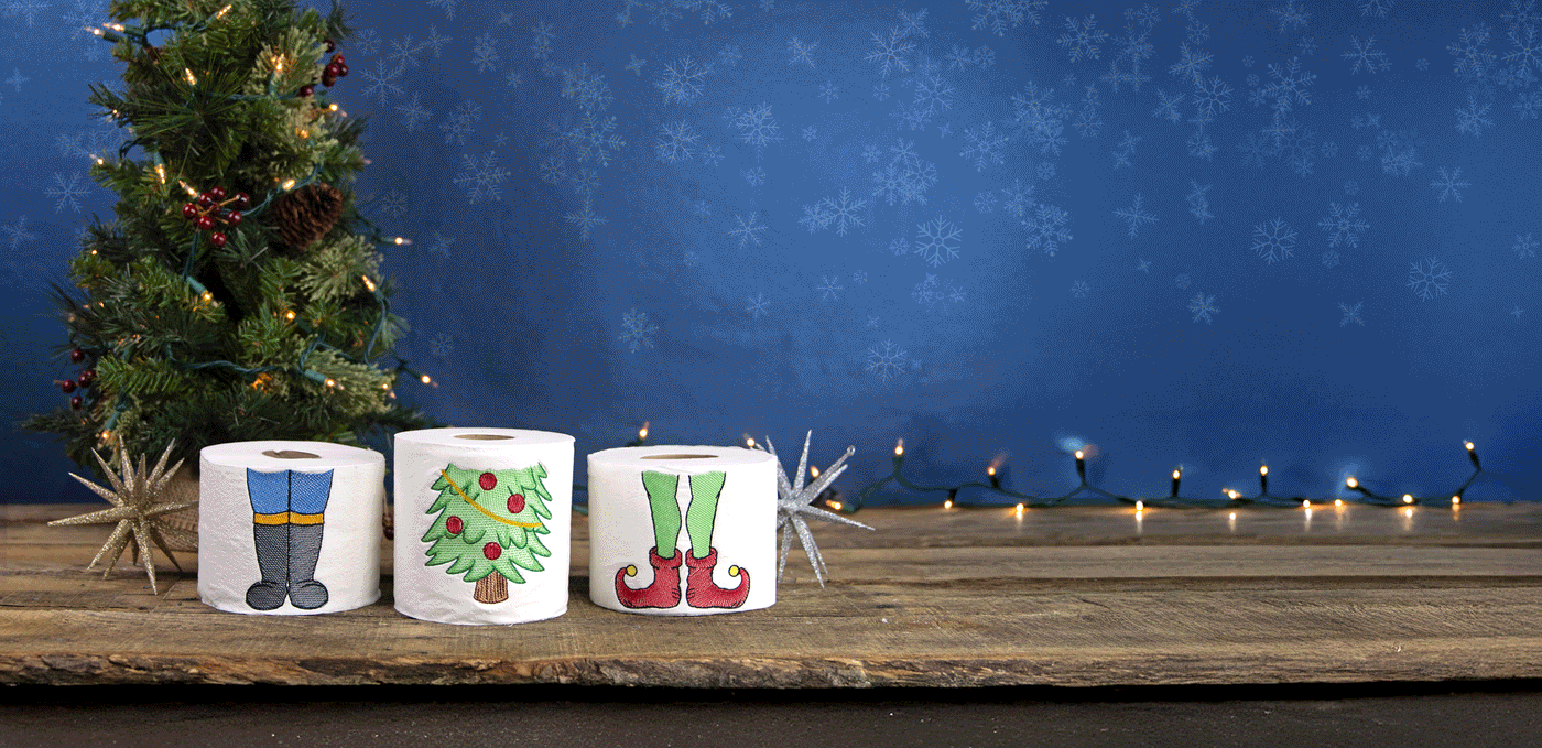 Gif of machine embroidery stackable toilet paper designs - nutcracker, tree, and elf on toilet paper on a wooden surface.