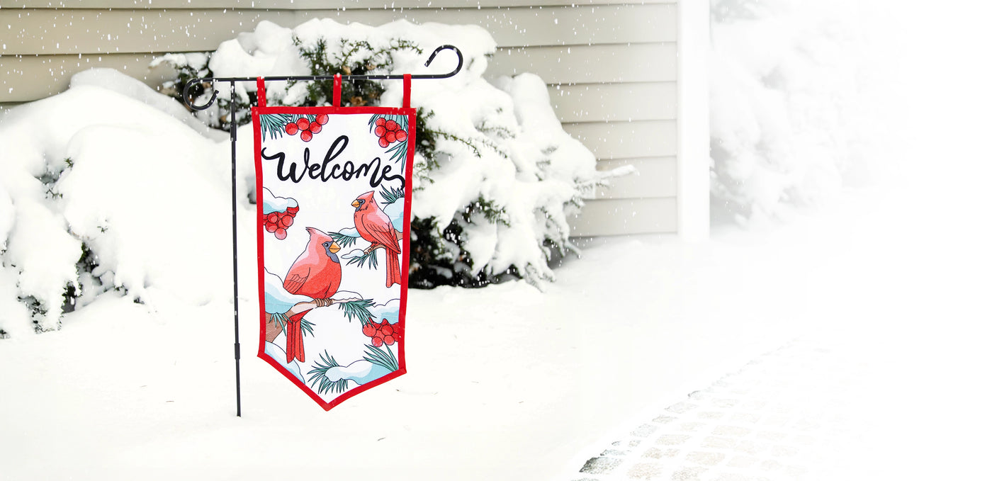 Decorative machine embroidery garden flag with winter design featuring cardinals and the word 'Welcome' in a snowy outdoor setting.