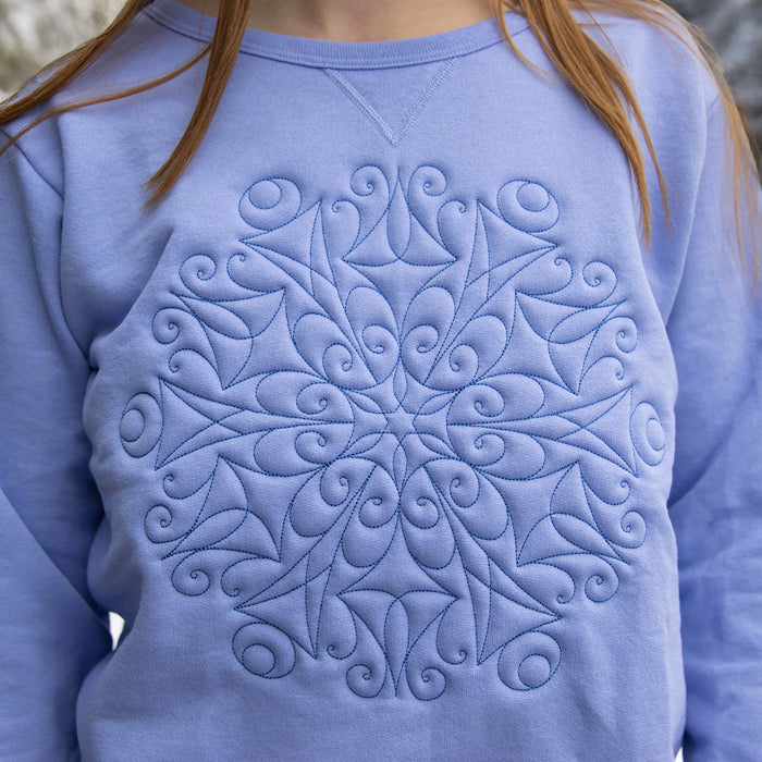 Close-up of a blue sweatshirt with a machine embroidery snowflake design on the chest.