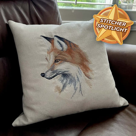 Machine embroidered fox pillow on a couch with 'Stitcher Spotlight' badge.