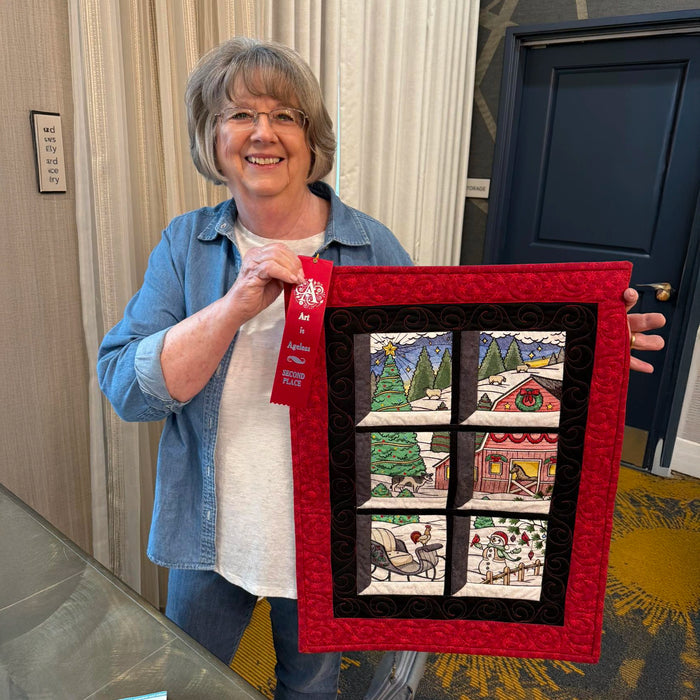 Woman holding a machine embroidery Christmas panel scene with an award ribbon.