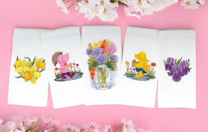 Spring themed machine embroidery designs on white towels, staged on a pink background.