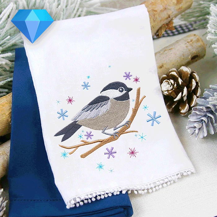 Embroidered chickadee bird on a branch with purple and blue snowflakes on a white towel over a navy towel.
