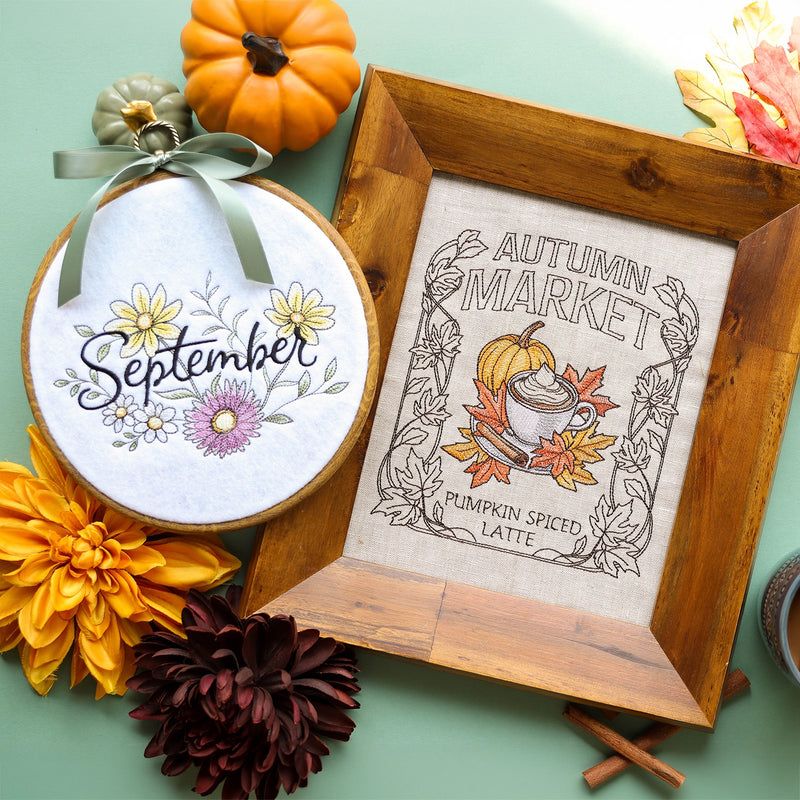 Two autumn-themed machine embroidery designs displayed on a mint green surface: a framed linen design reading 'Autumn Market Pumpkin Spiced Latte' with a pumpkin, leaves, and latte illustration, and an embroidery hoop with floral designs and the word 'September.' Decorative flowers, pumpkins, cinnamon sticks, and a wooden frame surround the items.