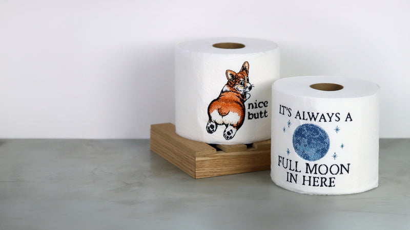 Two toilet paper rolls with machine embroidery corgi and moon design on a white background.