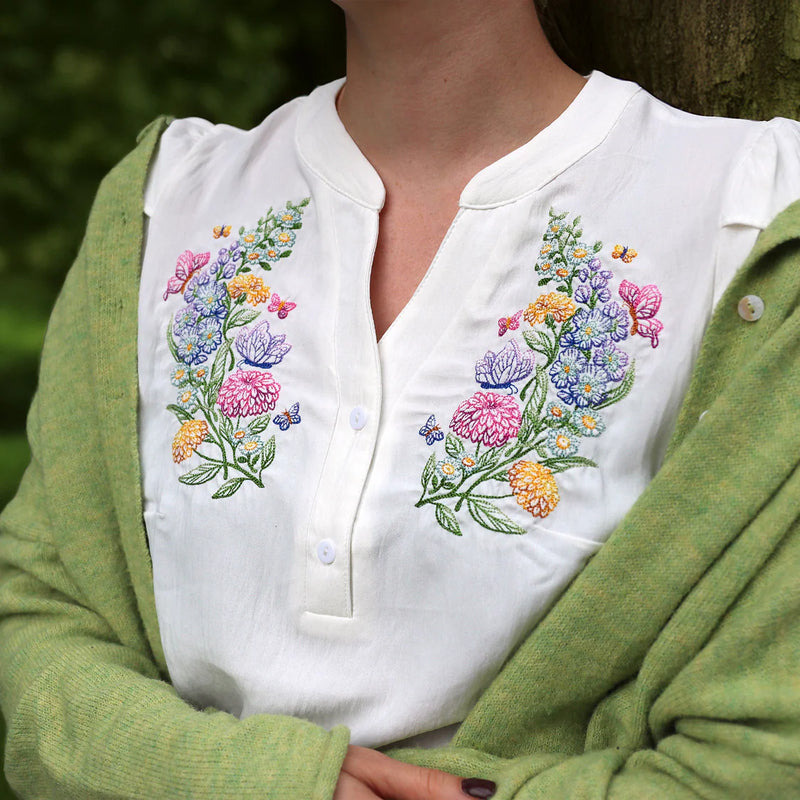 White blouse with machine embroidery floral design worn by a person in a green cardigan outdoors.