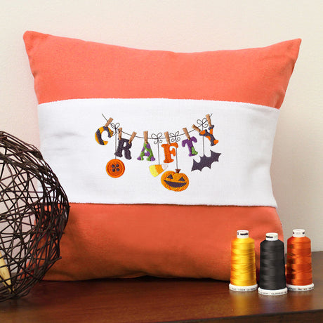 Halloween motifs embroidered in orange and black thread on a pillow, with visible stitching and decorative accents.