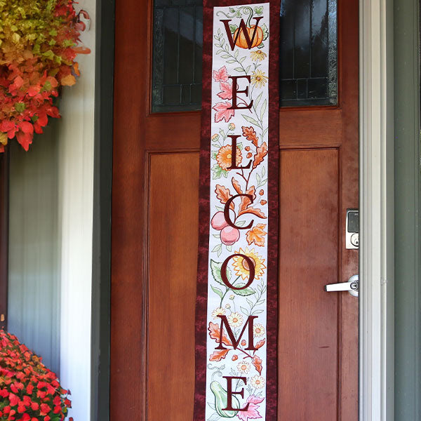 Decorative machine embroidered 'Welcome' sign with autumn leaves on a wooden door.