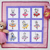 Embroidered quilt displays nine ballerinas in pink and purple borders with floral details, finished and clearly visible.