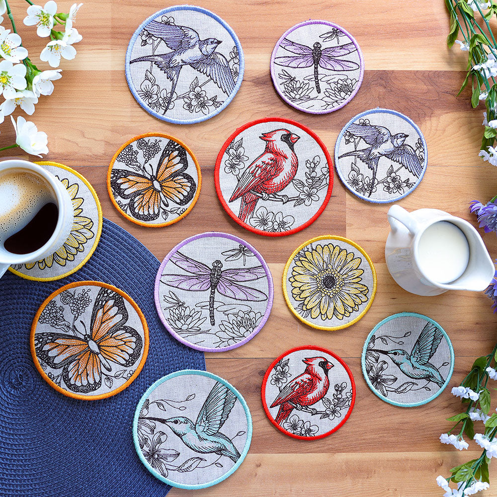 Set of decorative machine embroidered coasters with animal illustrations on a wooden table with a cup of coffee and milk pitcher.