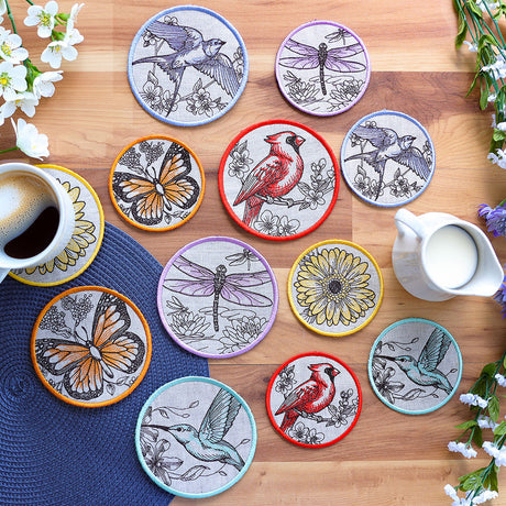 Set of decorative machine embroidered coasters with animal illustrations on a wooden table with a cup of coffee and milk pitcher.