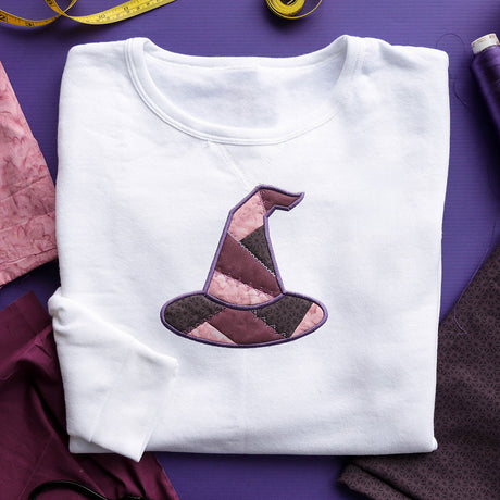 White sweatshirt with a digitally downloadable machine embroidery design of a colorful patchwork witch hat.