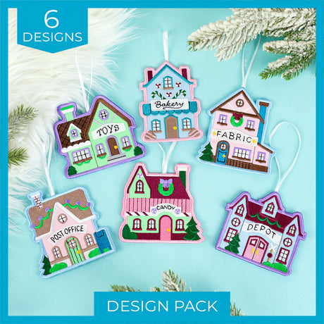 Six pastel-colored embroidered hanging house ornaments labeled Toys, Bakery, Fabric, Post Office, Candy, and Depot, displayed on a light blue background with pine branches.