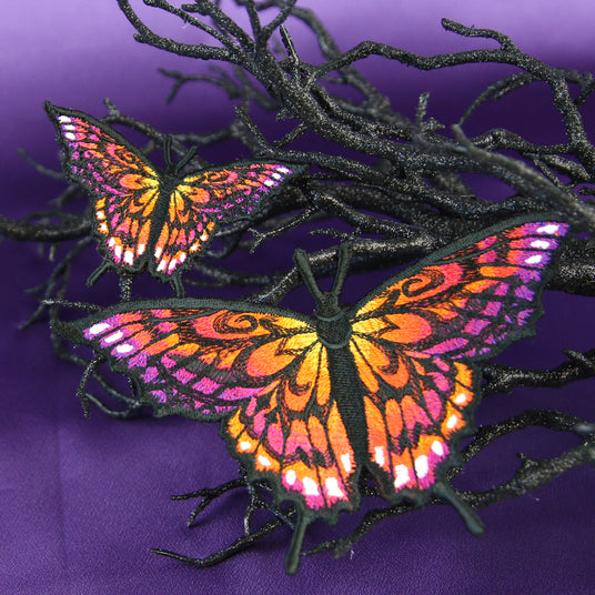 Two colorful butterfly patches on a branch against a purple background