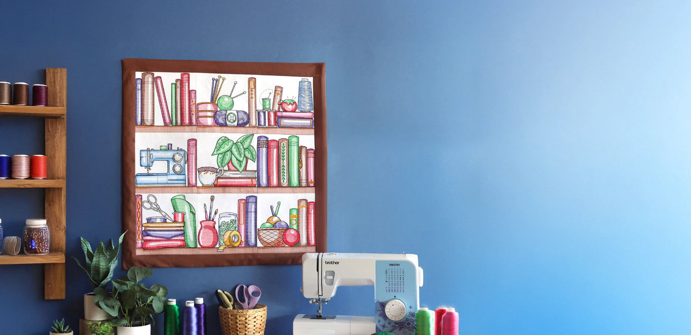 Sewing machine on a table with a machine embroidery bookshelf design on a blue wall.