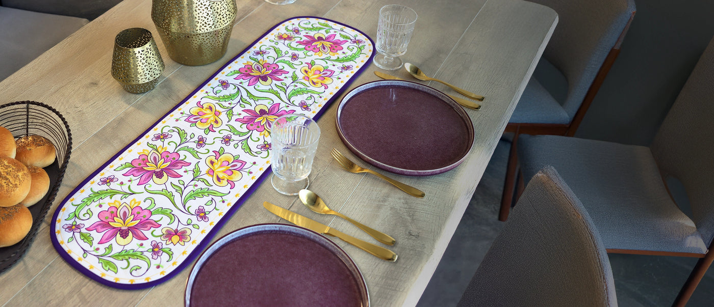 Dining table setting with floral machine embroidery designs on a table runner with plates and cutlery on a wooden table.