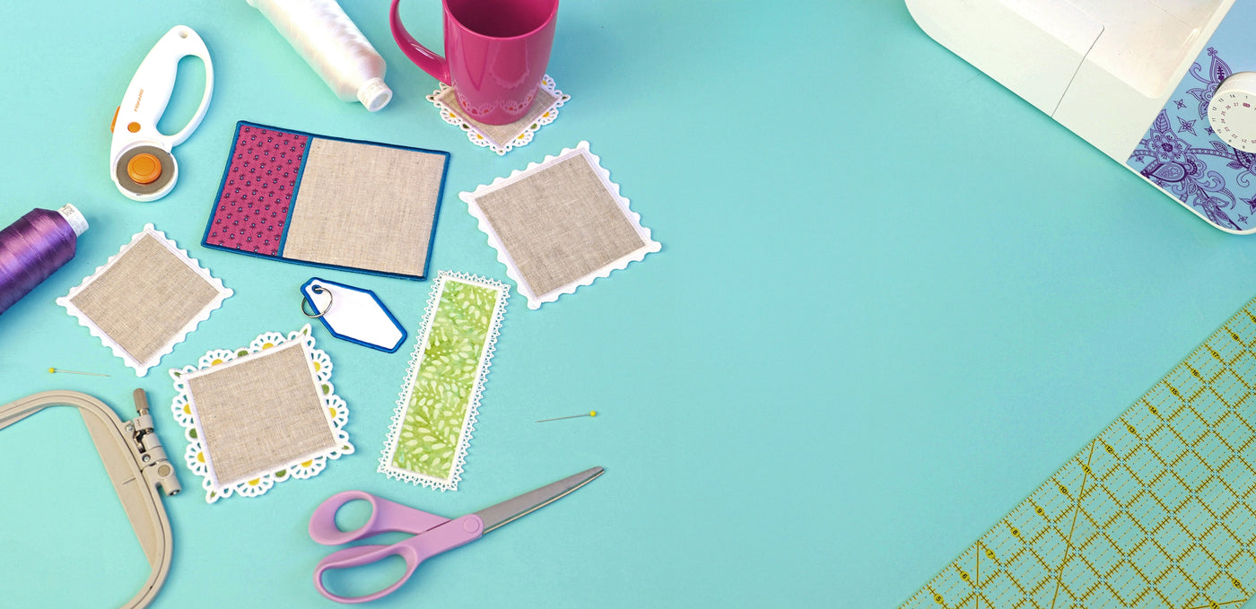 Machine embroidery blank designs including mug rug, coaster, keychain, bookmark and more on a blue background surrounded by crafting supplies.