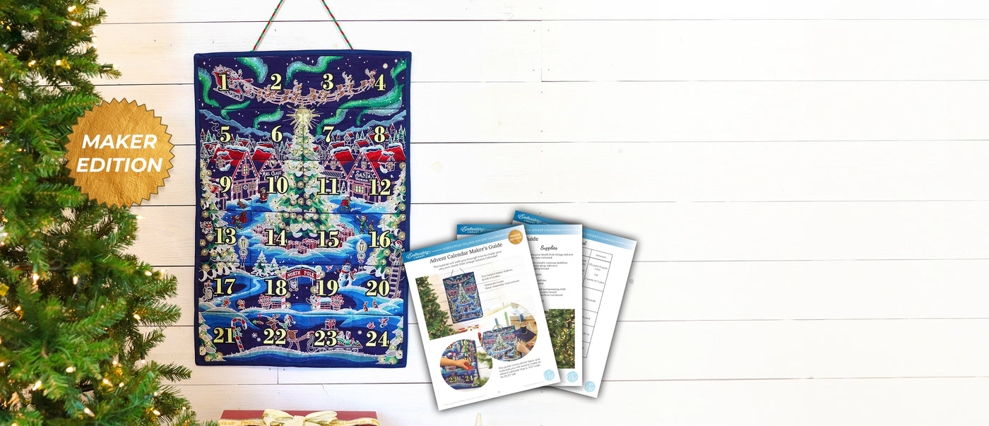 A hanging Christmas machine embroidered pocket advent calendar with a winter village scene and numbered days, shown beside printed PDF guide on a white wood background. A gold badge reads "MAKER EDITION," and part of a decorated tree is visible on the left.
