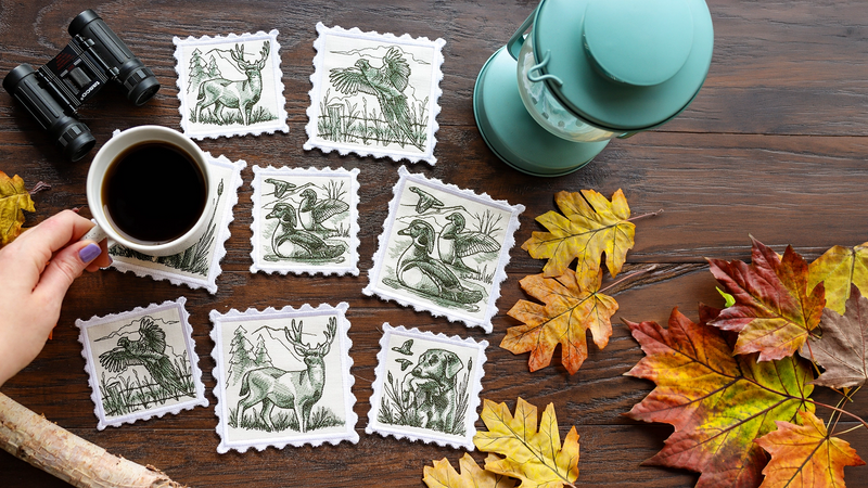 A set of eight white machine embroidered coasters with scalloped edges and dark green wildlife illustrations, arranged on a dark wooden table with autumn leaves, a mug of coffee, and a hand holding one coaster.