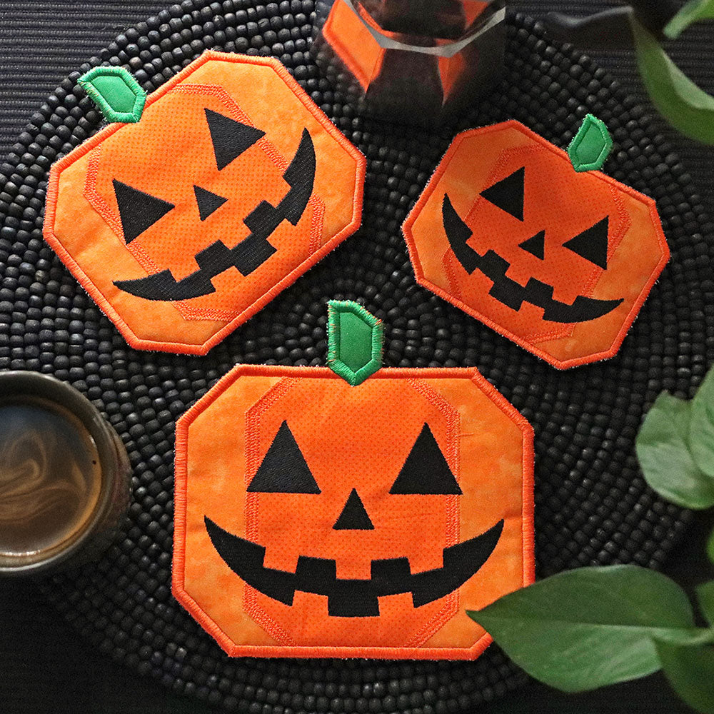 Three jack-o'-lantern trivet on a textured black surface with a cup and green leaves.
