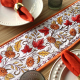 Machine embroidered autumn table runner with red, gold, and orange leaves and flowers, styled with orange napkins.