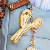 Yellow and white embroidered sewing scissors keychain design shown stitched on fabric, displayed as a finished project.