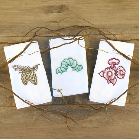 Digitally downloadable machine embroidery design featuring a pine cone on a branch, a green caterpillar, and a cluster of maroon flowers on white fabric.