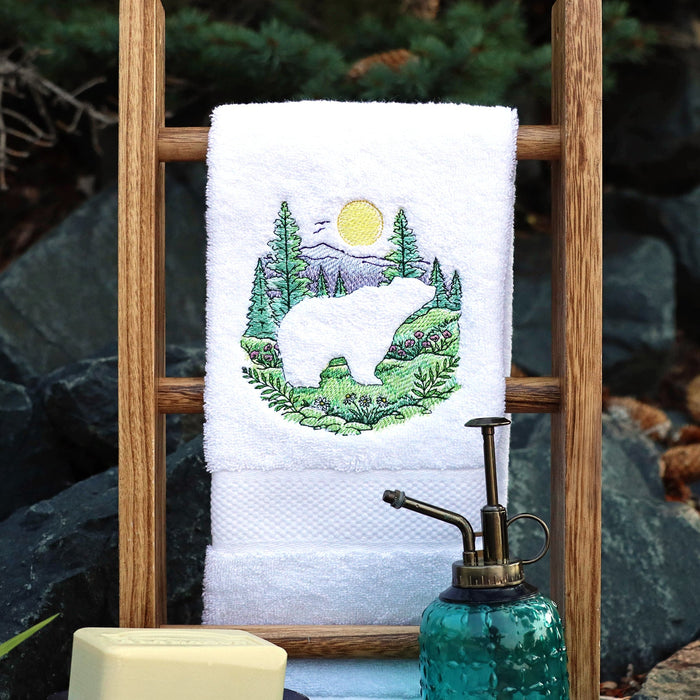 Towel with an embossed bear and forest design on a wooden stand against a natural rock background