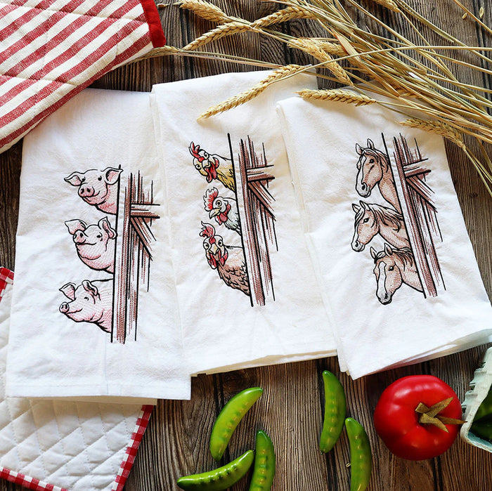 Farm animal embroidered tea towels featuring pigs, chickens, and horses peeking from barn doors, styled with wheat, vegetables, and rustic kitchen linens.