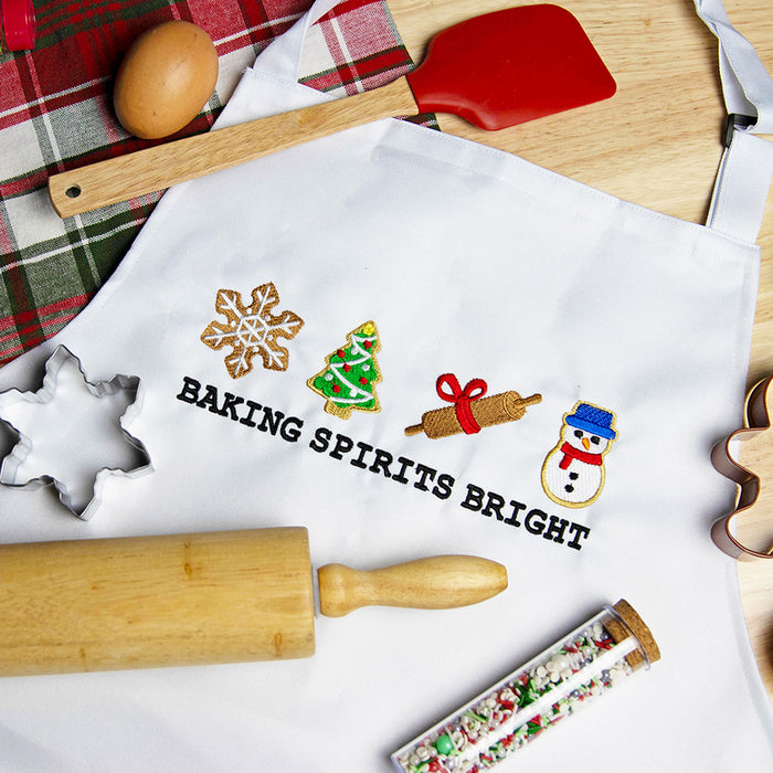 White apron with Christmas-themed machine embroidery design and text on a kitchen counter with baking tools.